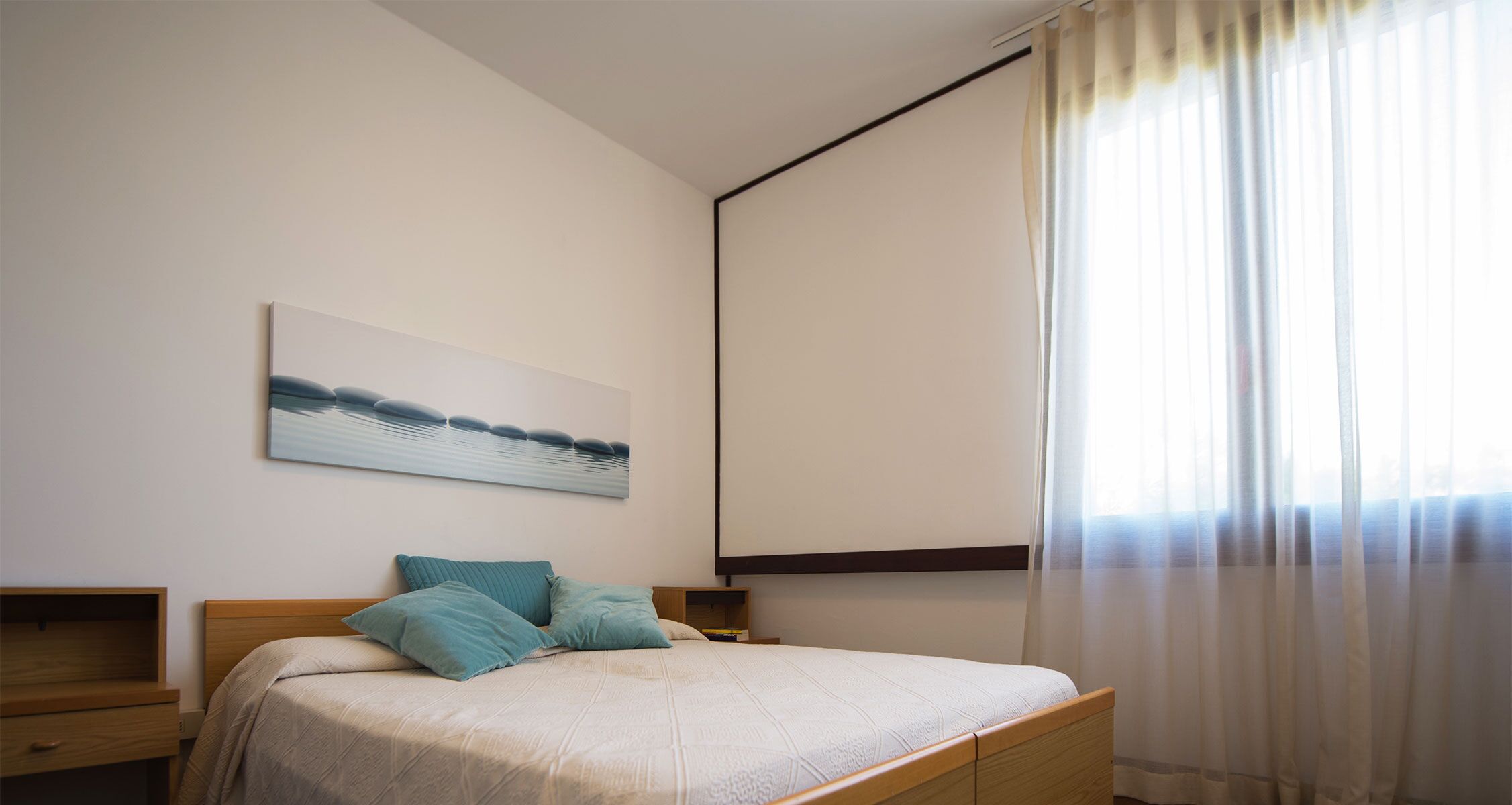 A bedroom with a bed, a nightstand, a painting, and a window with curtains.
