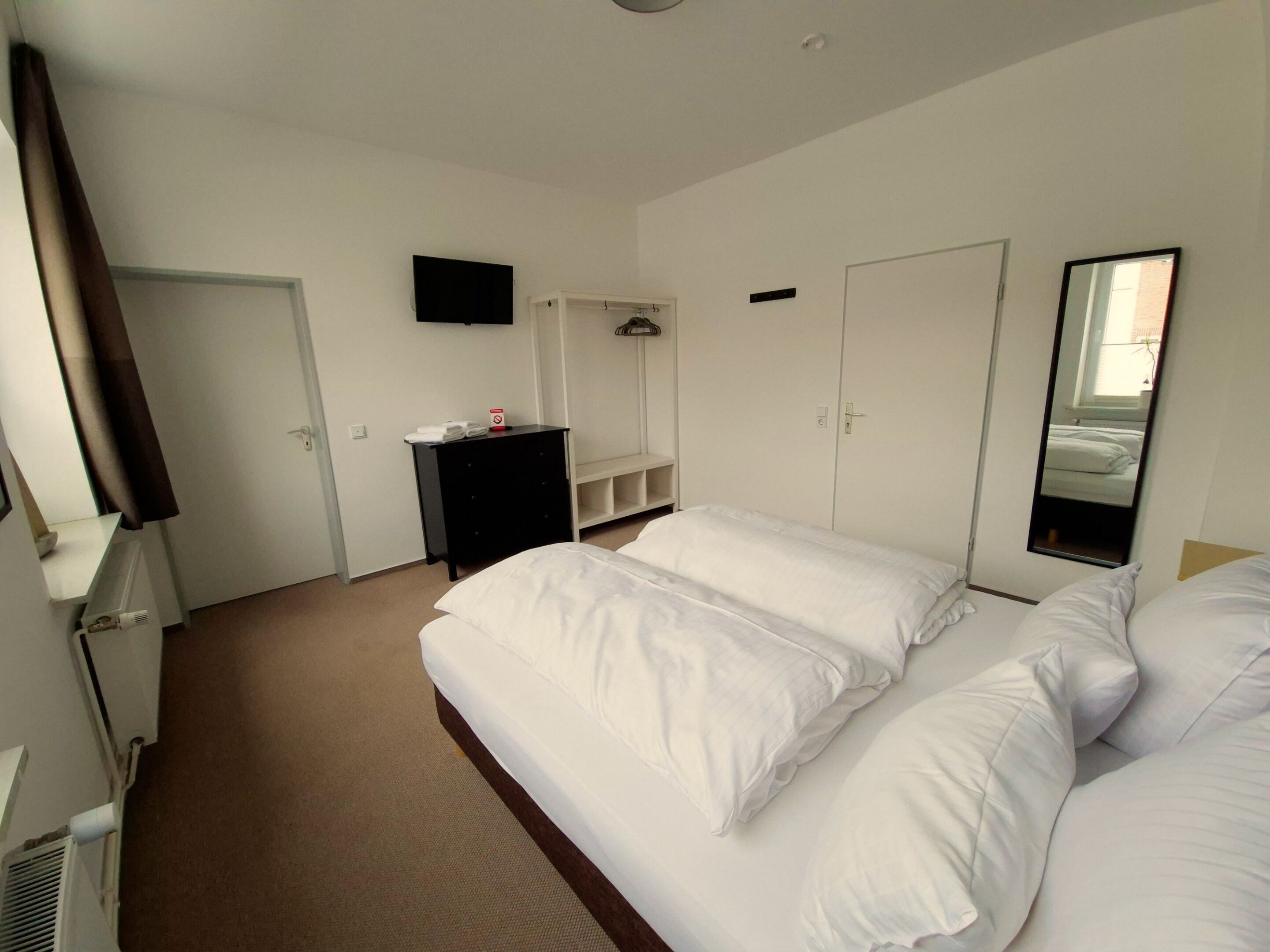 Una habitación de hotel con una cama grande, un televisor montado en la pared, un armario y un espejo.