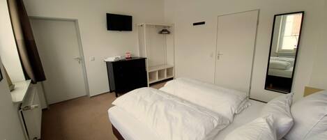 Una habitación de hotel con una cama grande, un televisor montado en la pared, un armario y un espejo.