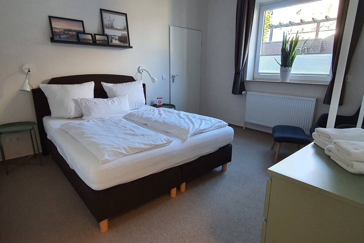 Habitación de hotel con cama, mesita de noche, silla y ventana con vistas.