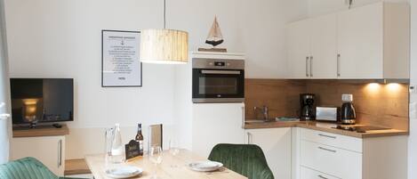 Una cocina moderna con armarios blancos, horno integrado, cafetera y un comedor con mesa y dos sillas.