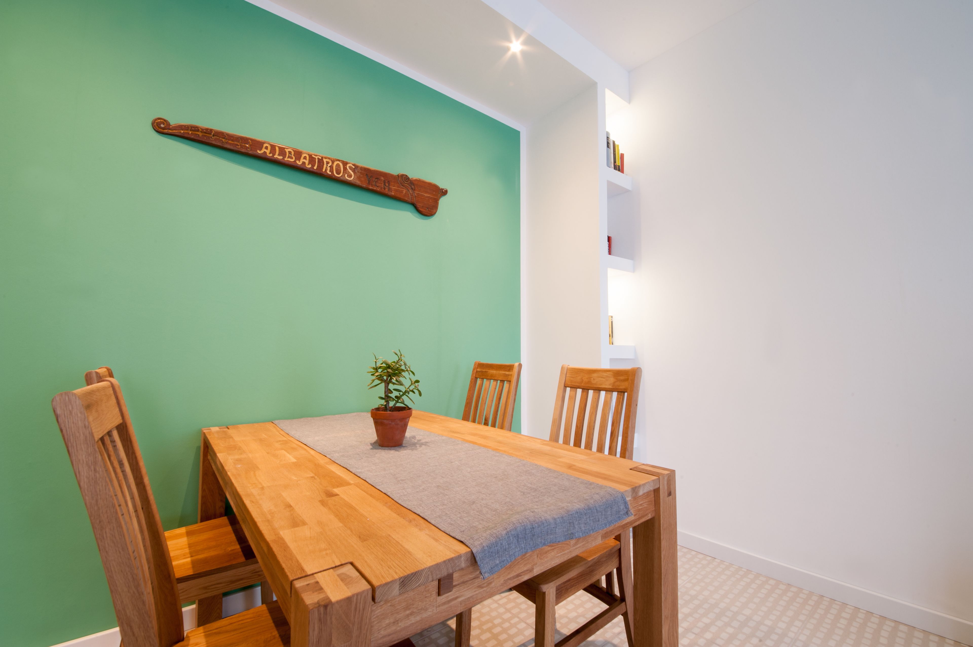 Un coin repas comprenant une table en bois, quatre chaises, une plante en pot et un panneau en bois fixé au mur.