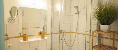 A bathroom with a glass-enclosed shower, a sink, a mirror, and a shelf with toiletries.