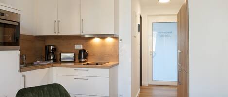 A modern kitchen with white cabinets, a wooden countertop, and a dining area with a green chair and a table set for two.