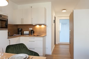 A modern kitchen with white cabinets, a wooden countertop, and a dining area with a green chair and a table set for two.