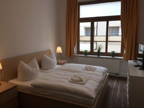 A hotel room with a bed, bedside tables, a desk, a TV, and a window with curtains. - Ferienwohnung Wittenberg (Lutherstadt Wittenberg)