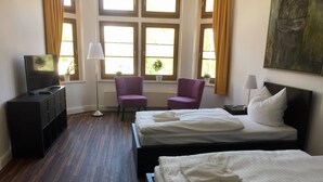 Een hotelkamer met twee bedden, een bureau met een televisie, een stoel en een vloerlamp.