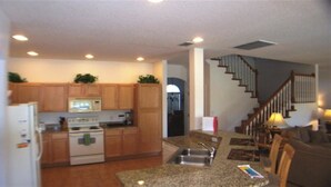 A kitchen with wooden cabinets, a microwave, a stove, and a sink. There is a staircase leading to another level. - Ov3125 - Highlands Reserve - 6 Bed 4 Baths Villa (Davenport)