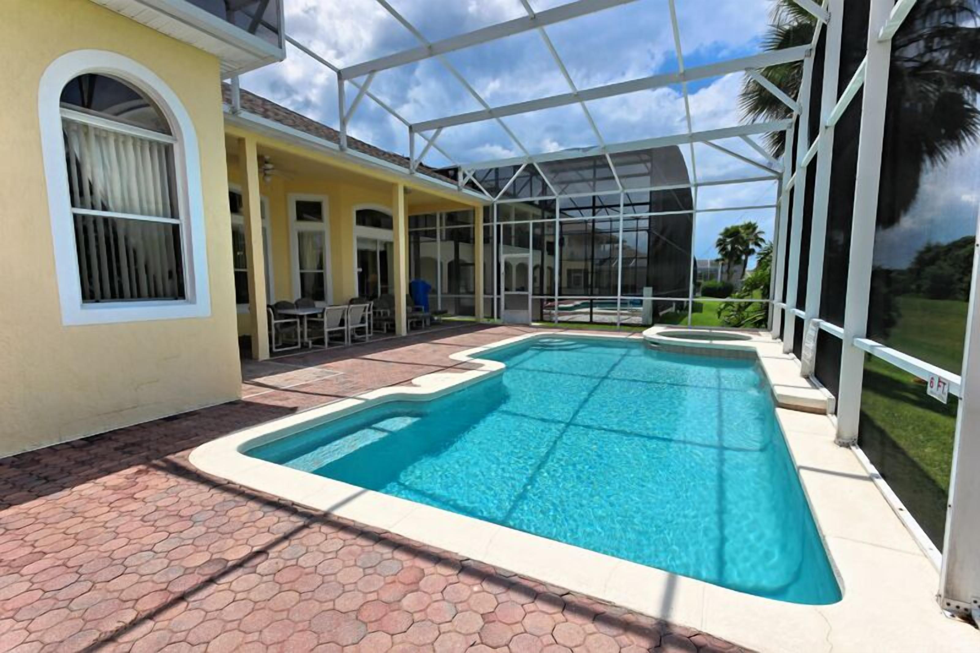 A pool area with a glass enclosure, a patio with hexagonal tiles, and a view of the surrounding landscape.