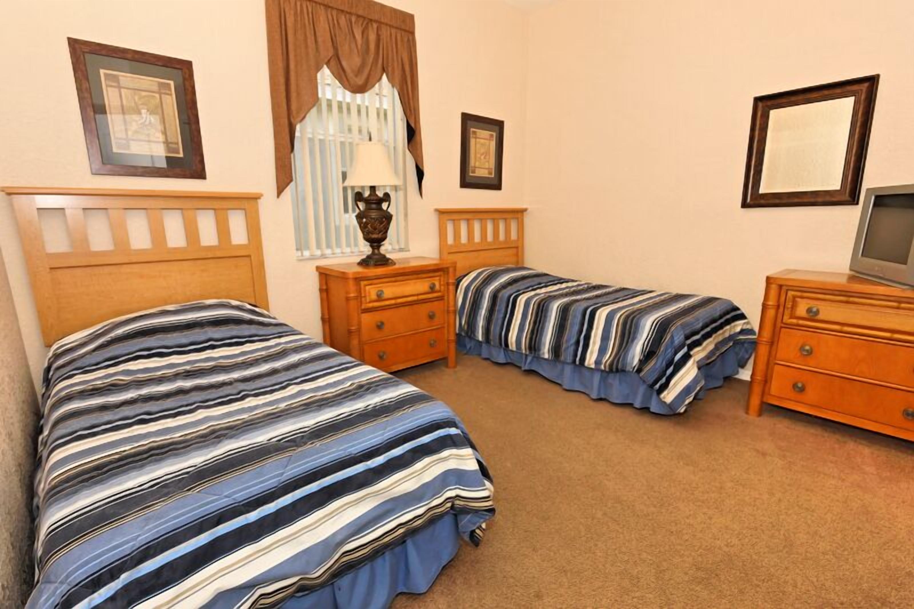 A bedroom with two beds, a nightstand with a lamp, a dresser, and a television.