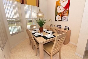 Ein Essbereich mit einem Tisch für vier Personen, Holzsesseln, einem Blumentopf und einer Pendelleuchte.