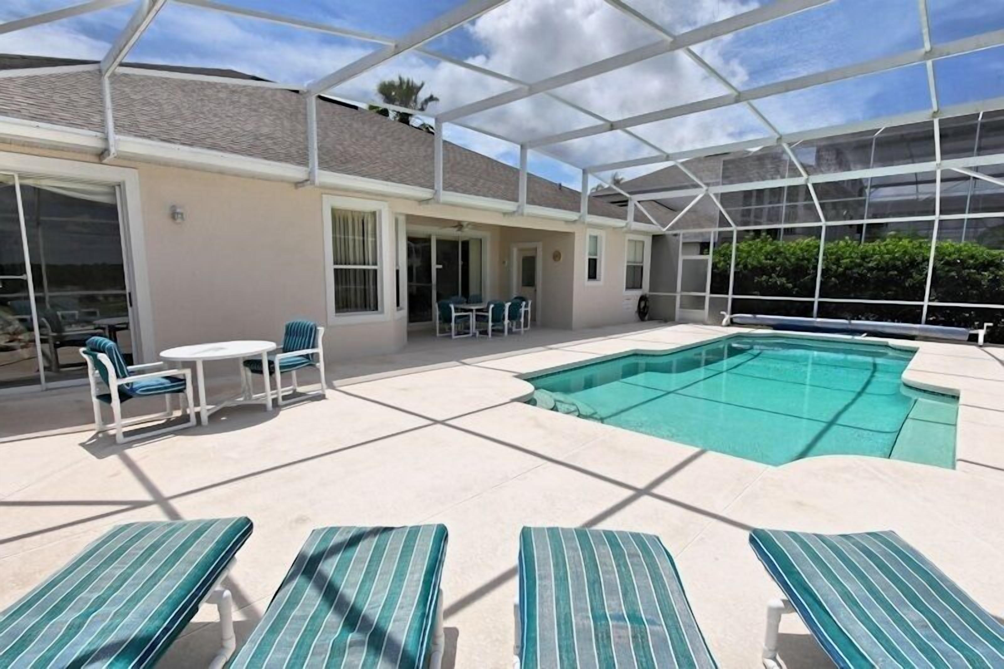 A covered outdoor swimming pool area with lounge chairs and a table.
