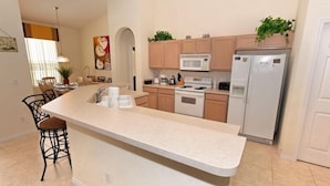 Una cocina moderna con una isla central, armarios de madera, microondas, estufa y refrigerador.
