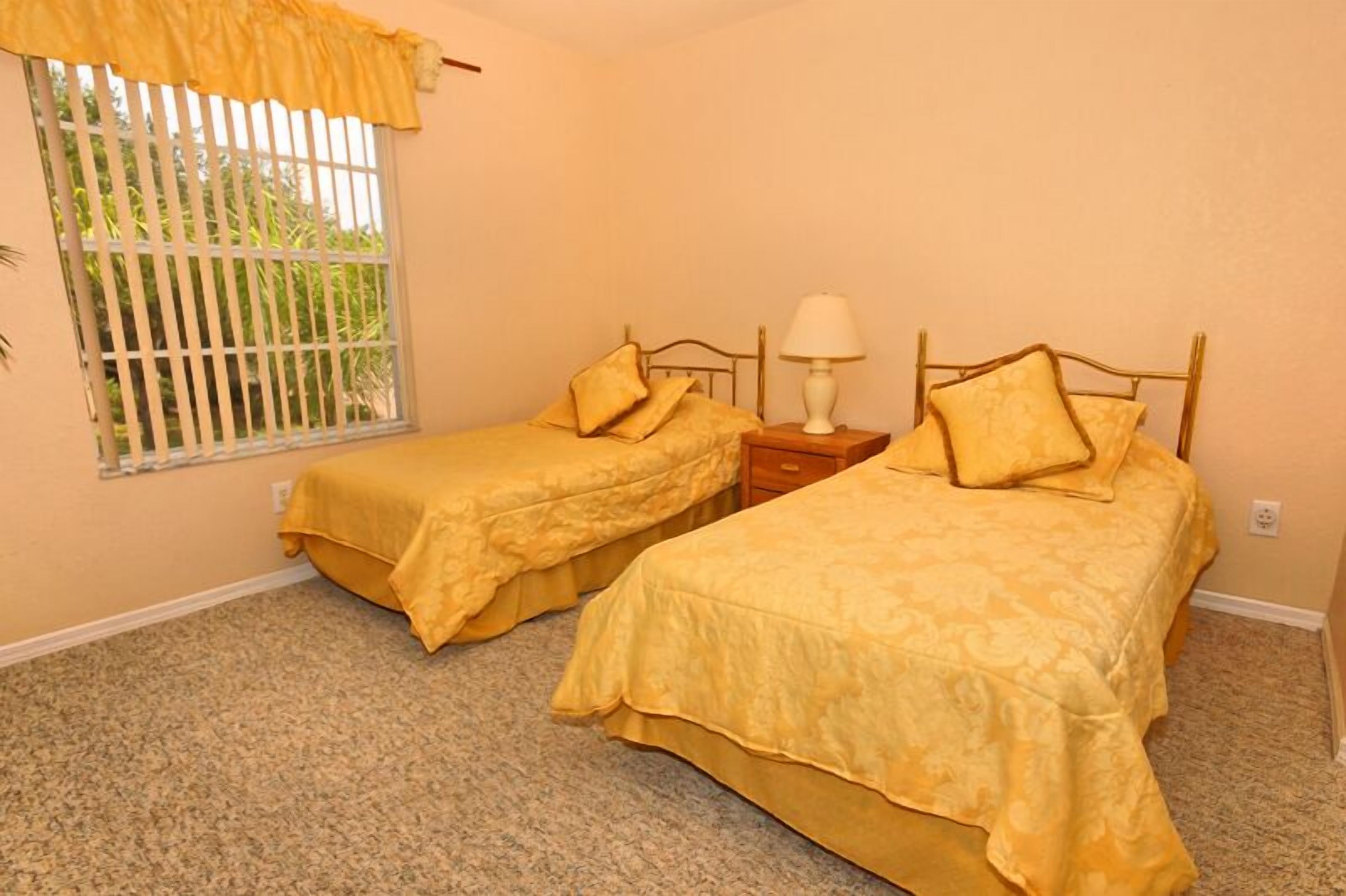 Una habitación con dos camas individuales, una mesita de noche con lámpara y una ventana con barrotes.