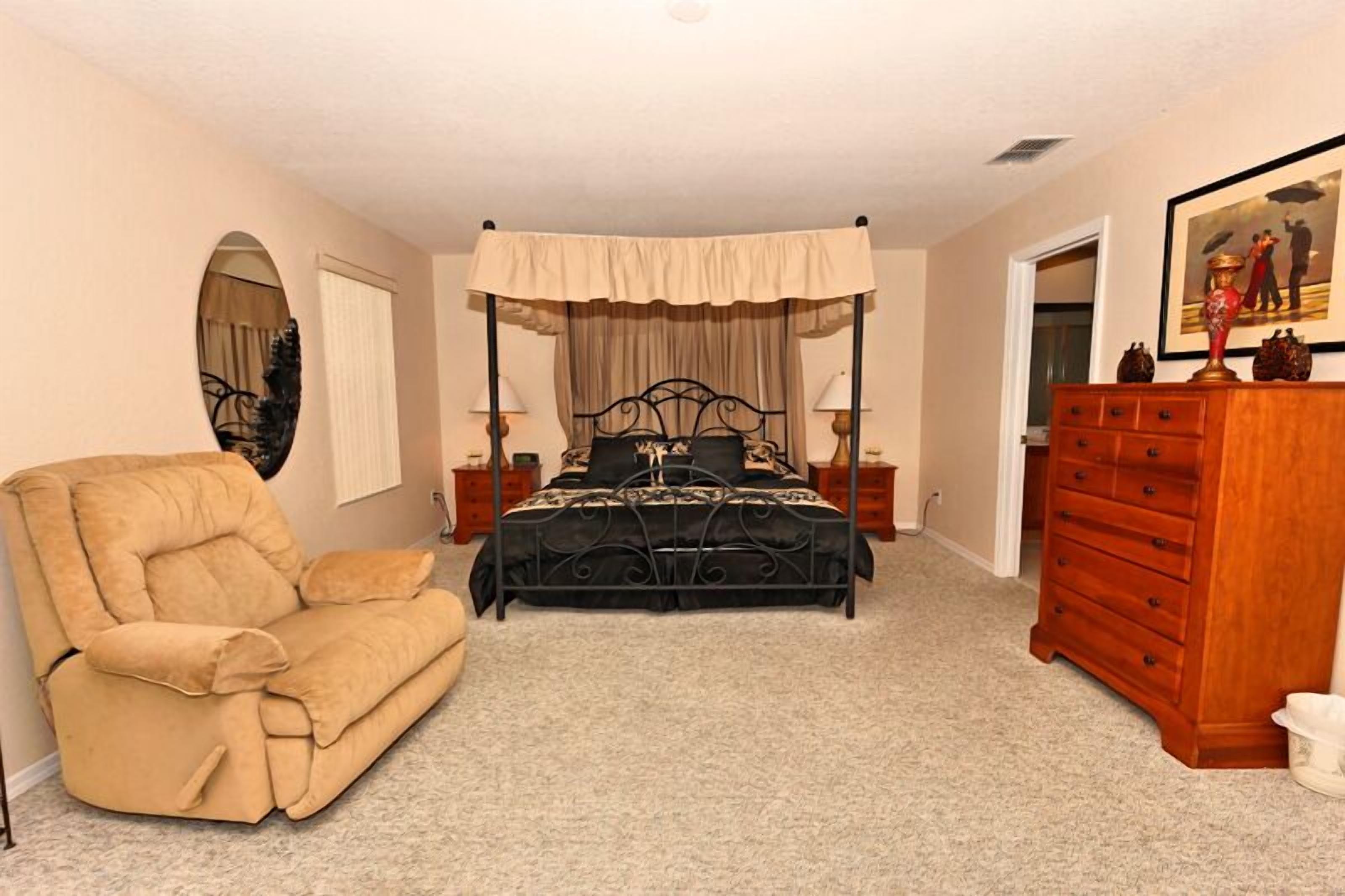 A bedroom with a four-poster bed, a chaise lounge, a wooden dresser, and a mirror.