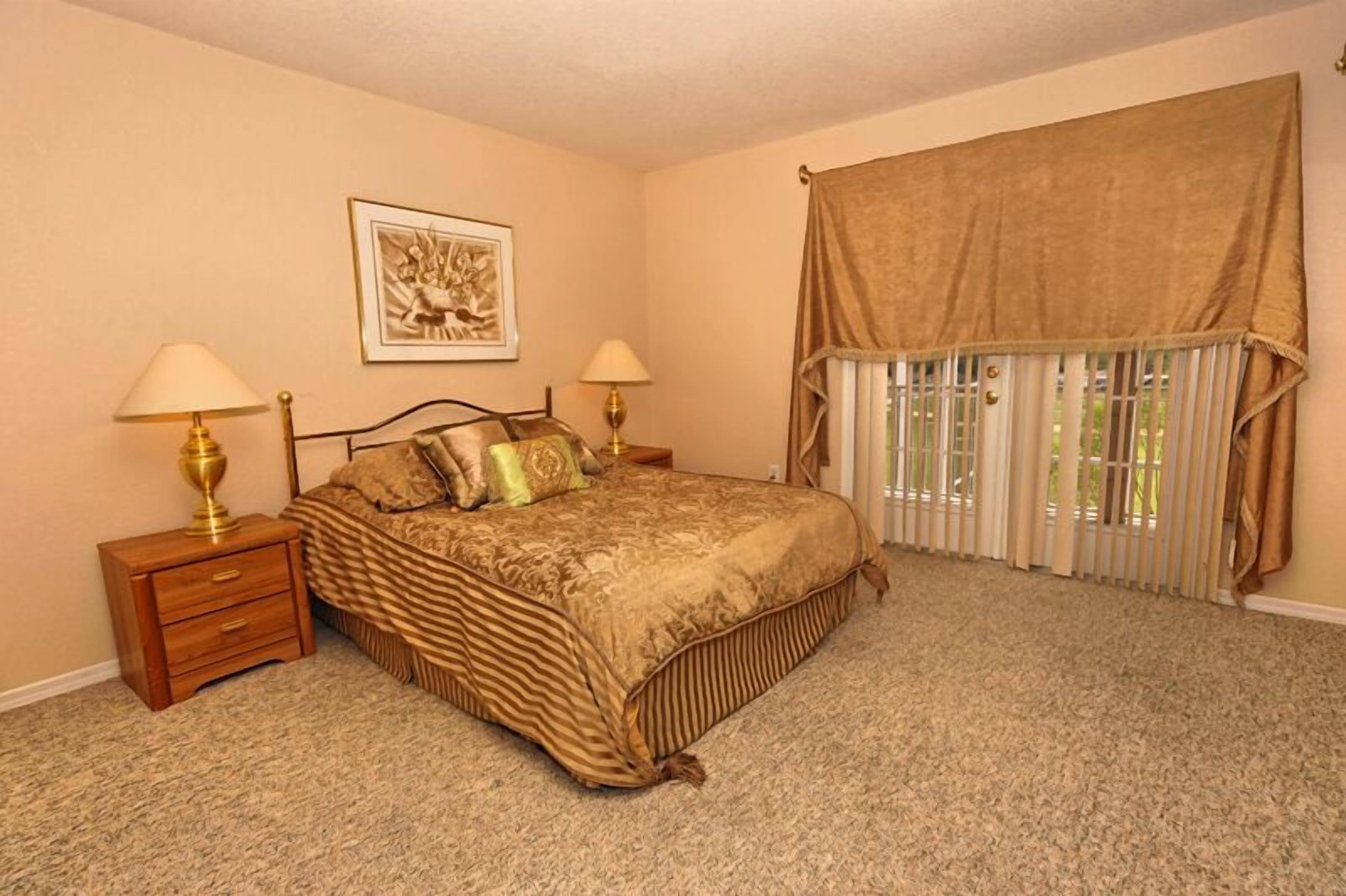 A bedroom with a large bed, two bedside tables, a framed picture on the wall, and a window with curtains.