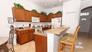 Una cocina con armarios de madera, microondas, estufa, lavaplatos y una barra con una silla.