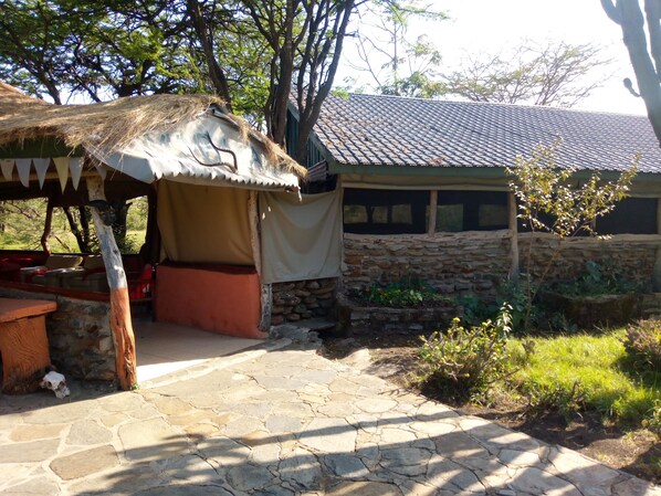 A stone building with a thatched roof structure adjacent to it. - Nyumbu Camp (Maasai Mara)