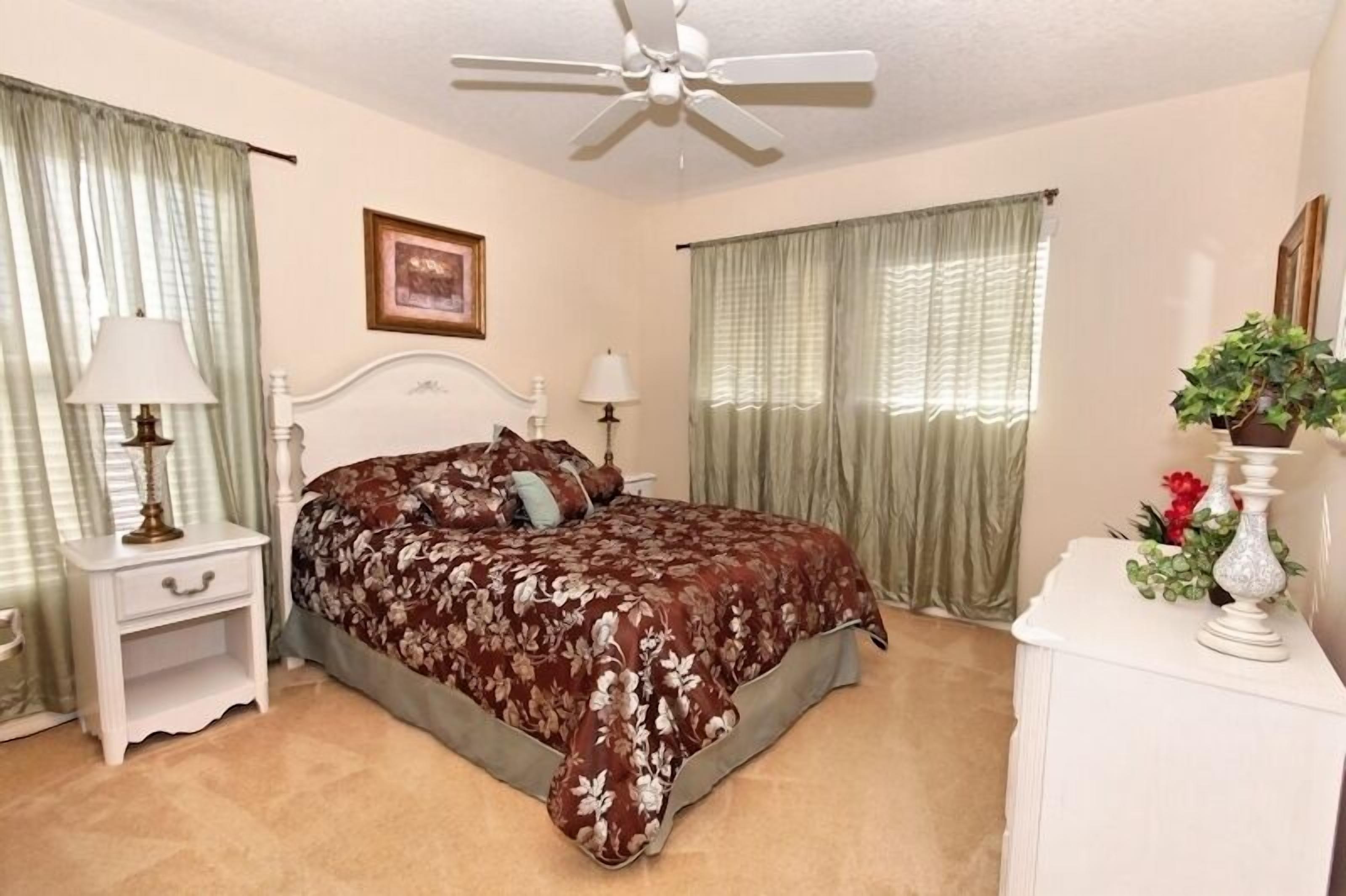 A bedroom with a bed, nightstands, a ceiling fan, and curtains.