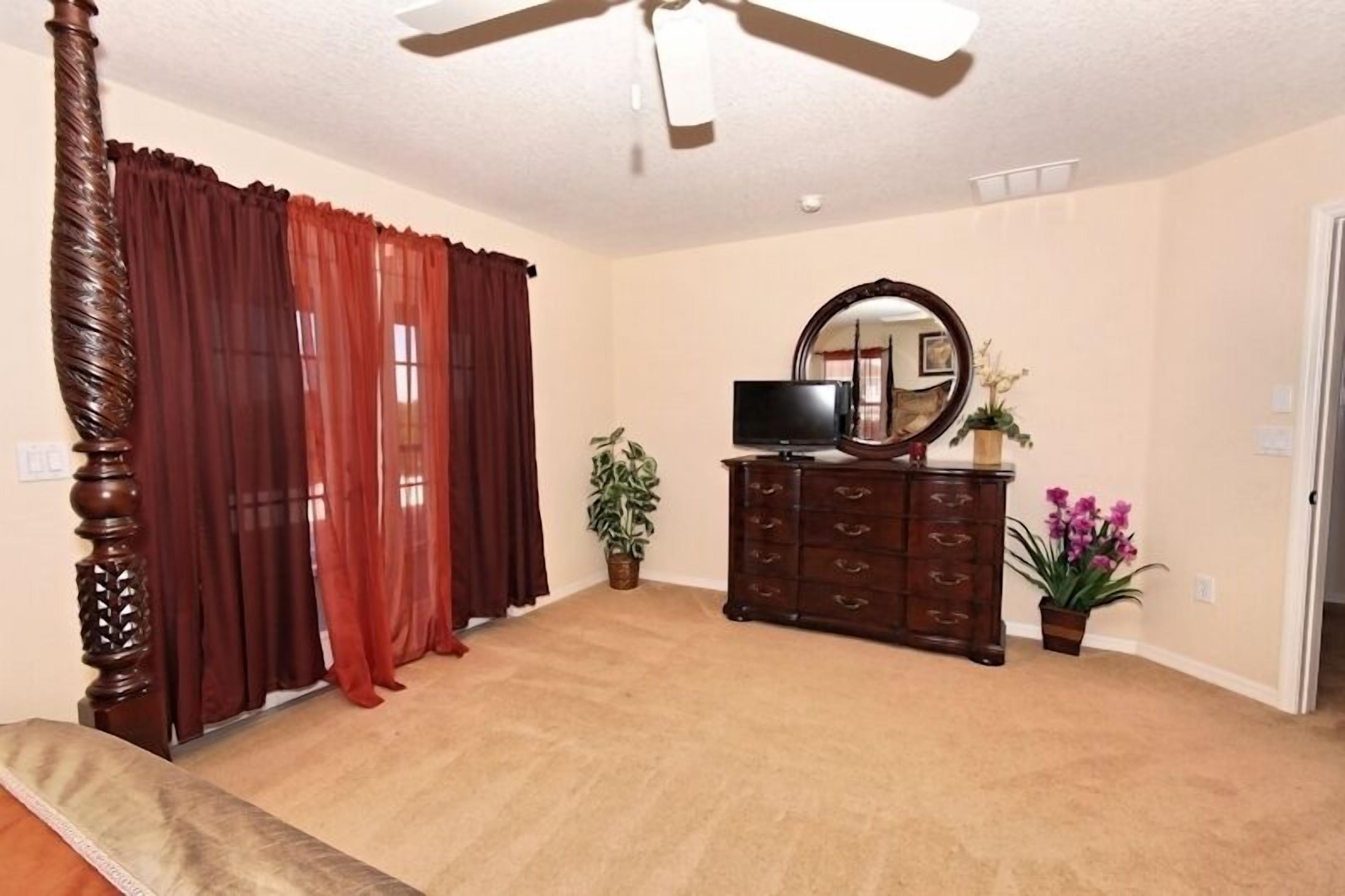 A room with a ceiling fan, a television on a dresser, a mirror, and two potted plants.