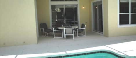 A covered patio with a pool, a table with chairs, and a sliding glass door.