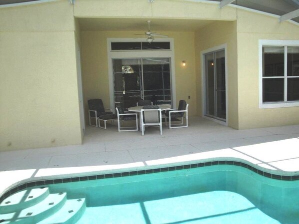 Un patio techado con piscina, una mesa y sillas, y una puerta corrediza de vidrio.