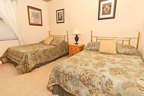 Une chambre avec deux lits, chacun agrémenté de draps à motifs floraux, une table de chevet avec une lampe et des œuvres d’art encadrées accrochées aux murs.