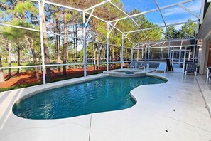 Une piscine dotée d’une structure en verre, entourée d’arbres et agrémentée d’un espace de détente extérieur.