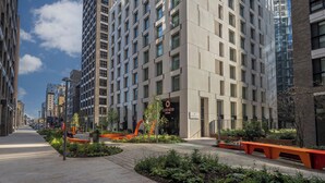 Egy modern hotel, letisztult, geometrikus homlokzattal, nagy ablakokkal, valamint gondozott, kültéri területettel, ahol ülőhelyek és növények találhatóak.