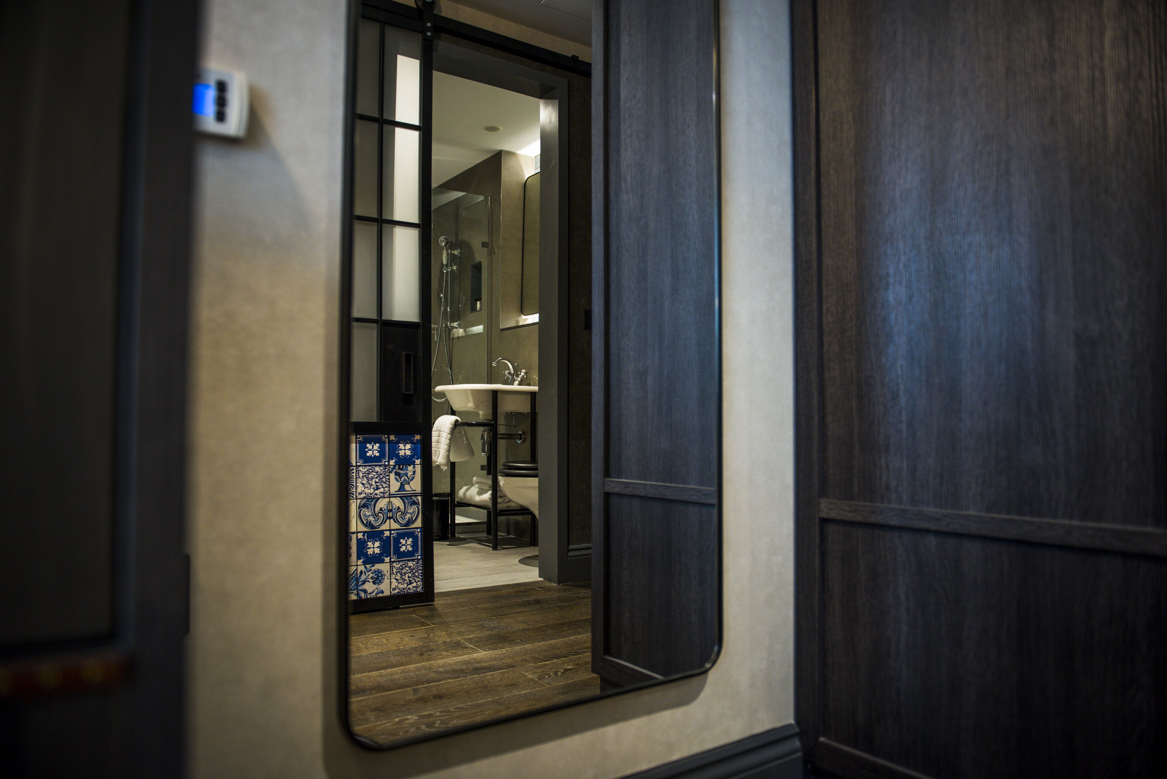 Une chambre d’hôtel avec un plancher en bois, une salle de bain avec un lavabo blanc et un mur recouvert de carreaux.