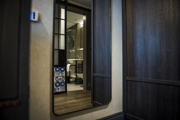 Habitación de hotel con piso de madera, baño con lavamanos blanco y salpicadero de azulejos.