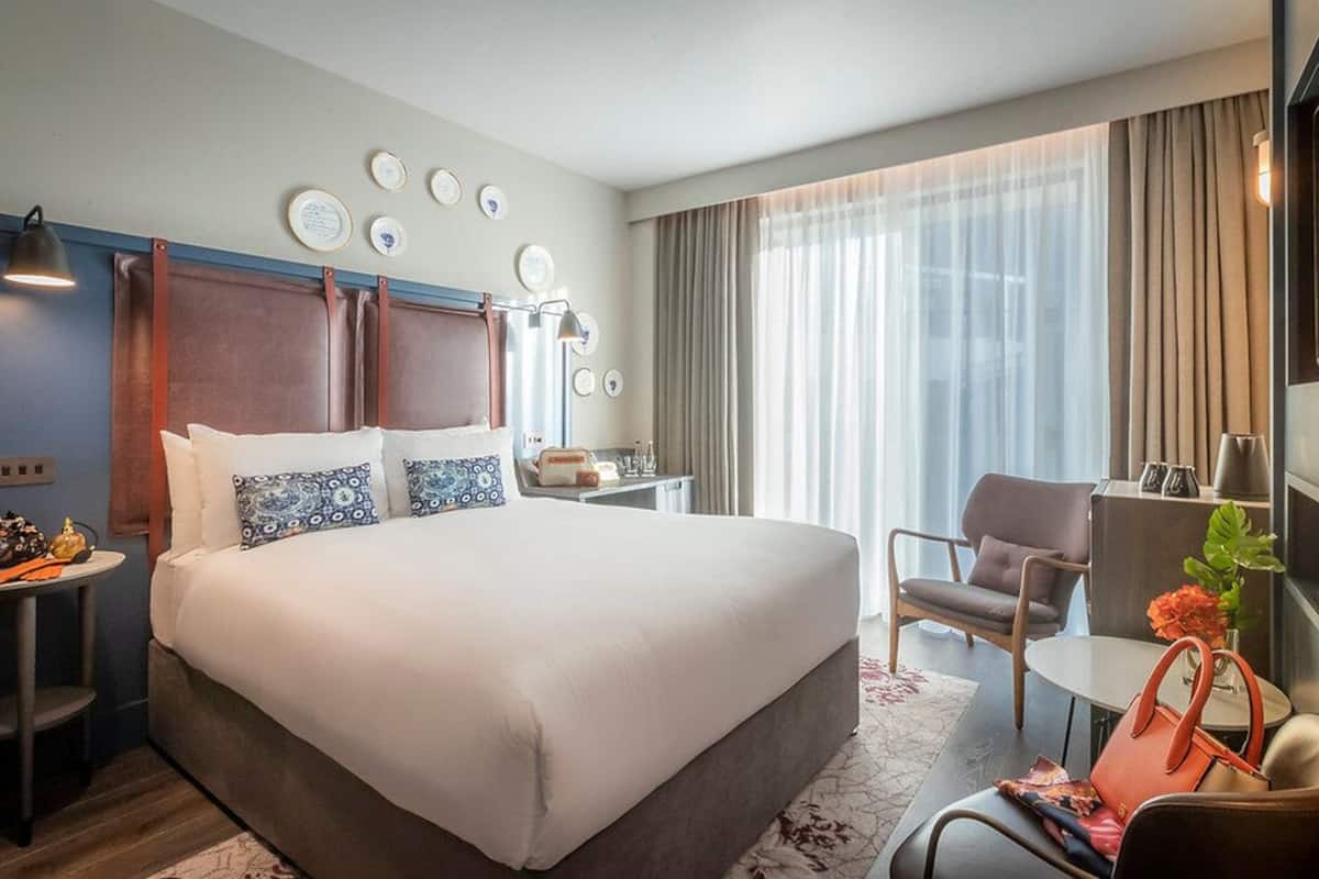 A hotel room with a large bed, a desk, a chair, and a small table.