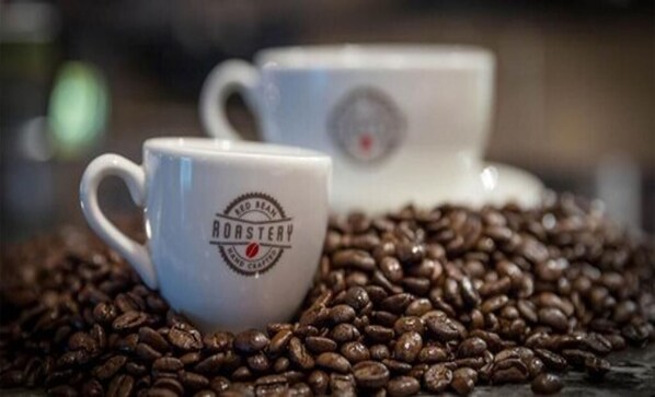 Two white coffee cups with a logo on them, surrounded by coffee beans.