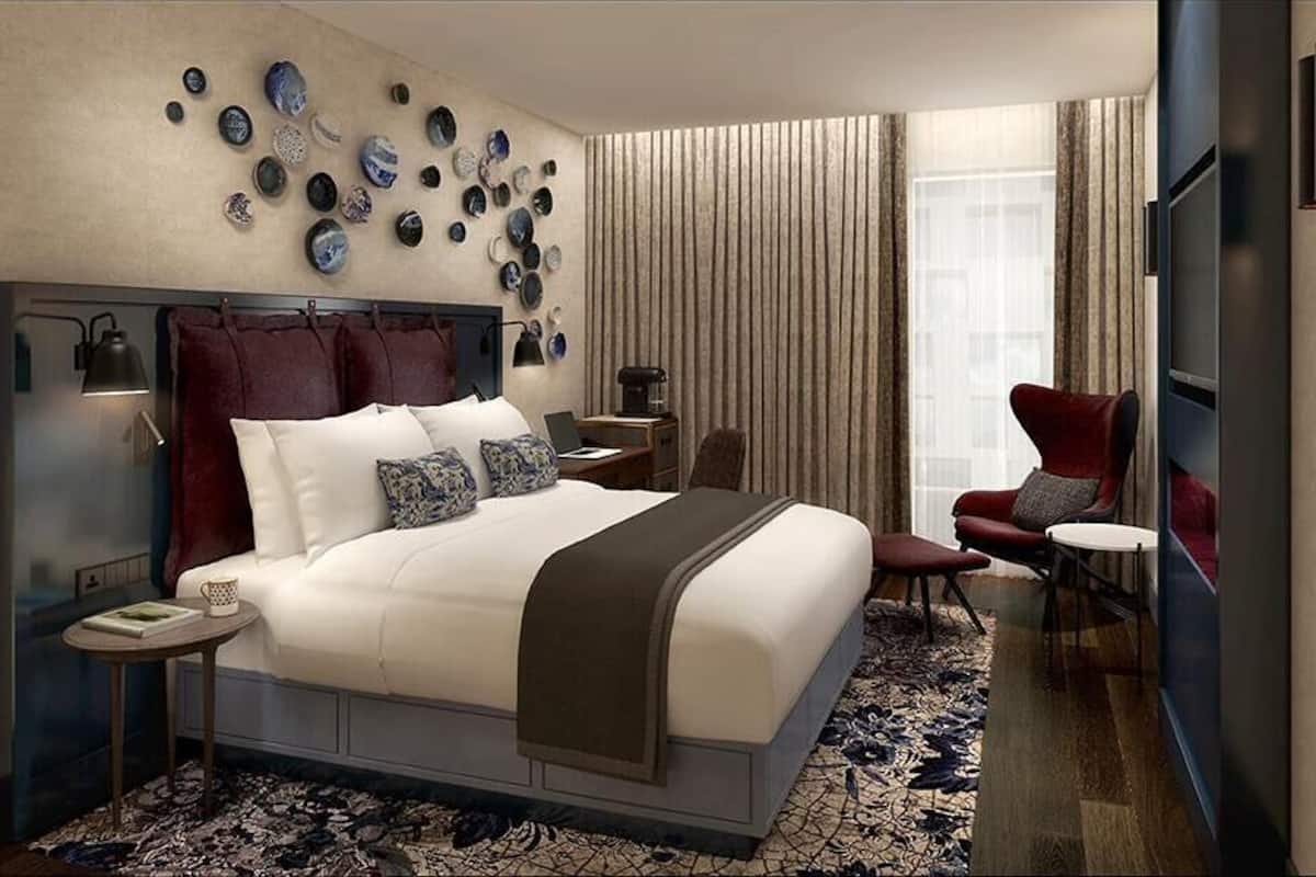 A modern hotel room with a large bed, a desk, a chair, and a TV.