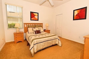 A bedroom with a bed, two bedside tables, a window with blinds, and two framed pictures on the walls.