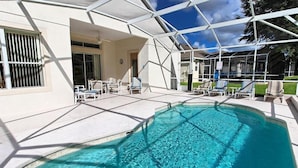 A swimming pool with clear water, surrounded by a covered patio area with lounge chairs and a building with large windows. - Ov3102 - Highlands Reserve - 4 Bed 3 Baths Villa (Davenport)