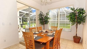 A dining area with a wooden table and chairs, a potted plant, and a view of a greenhouse through large windows. - Ov3102 - Highlands Reserve - 4 Bed 3 Baths Villa (Davenport)