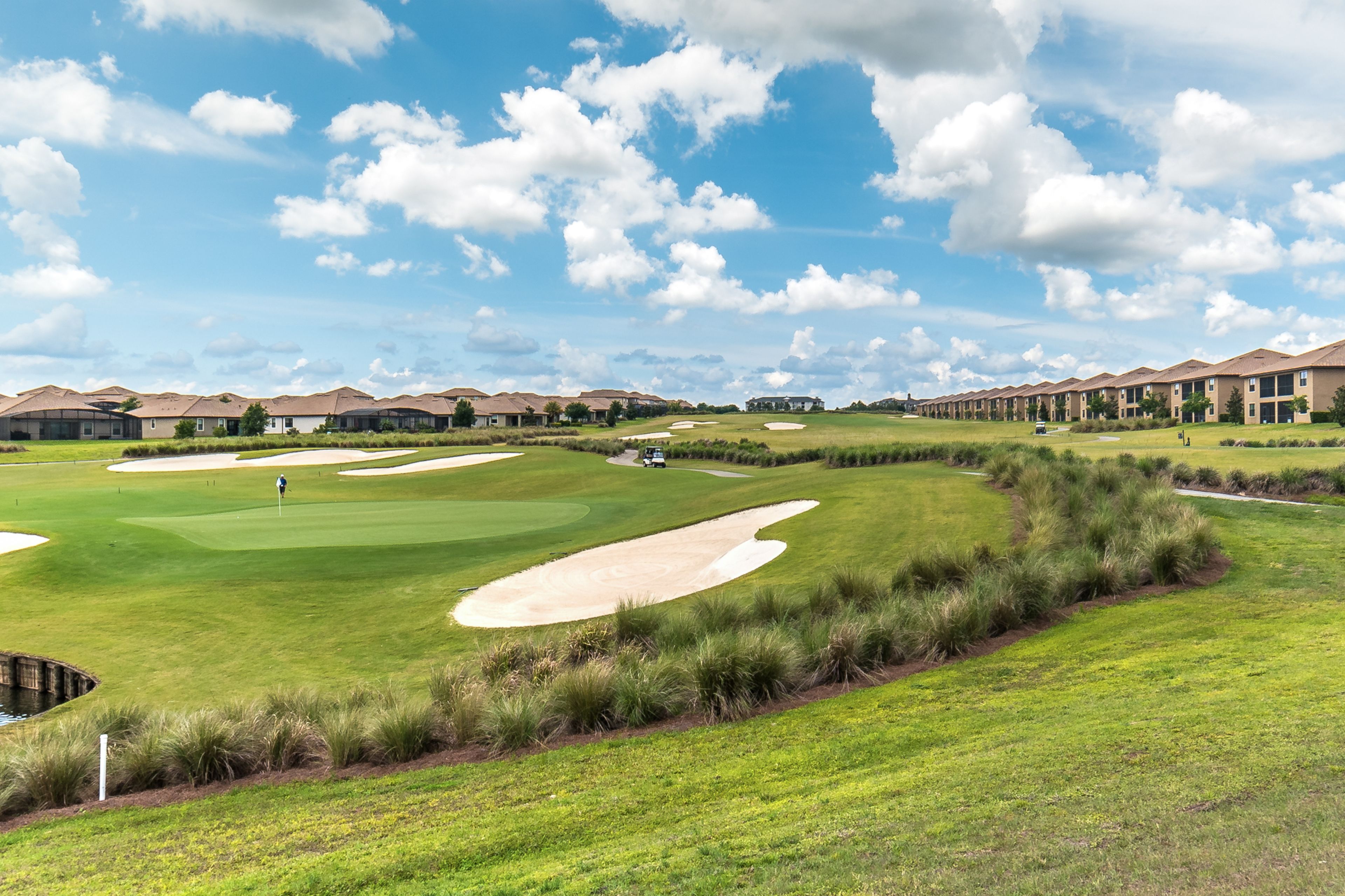 A golf course with bunkers, a putting green, and a clubhouse in the background.