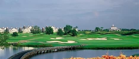 A golf course with a water body, a bridge, and a clubhouse in the background.