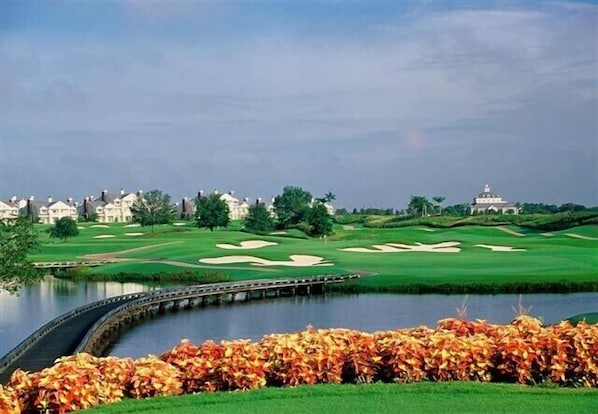 A golf course with a water body, a bridge, and a clubhouse in the background.
