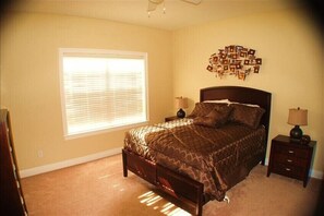 A bedroom with a bed, a nightstand, a lamp, a window with blinds, and a wall decoration.