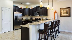 A modern kitchen with dark cabinets, stainless steel appliances, a granite countertop, and pendant lighting. - Ov3060 - Champions Gate Resort - 8 Bed 5 Baths Villa (Davenport)