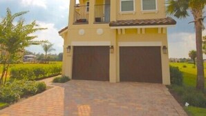 Une maison à deux étages avec un balcon, deux garages et une allée pavée.