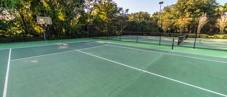 A tennis court with a net, surrounded by trees and a fence.