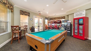 A pool table with a green felt surface, surrounded by wooden chairs and a small table. There are arcade machines and an ATM machine in the background. - Ov3007 - Windsor Hills Resort - 3 Bed 3 Baths Townhome (Kissimmee)