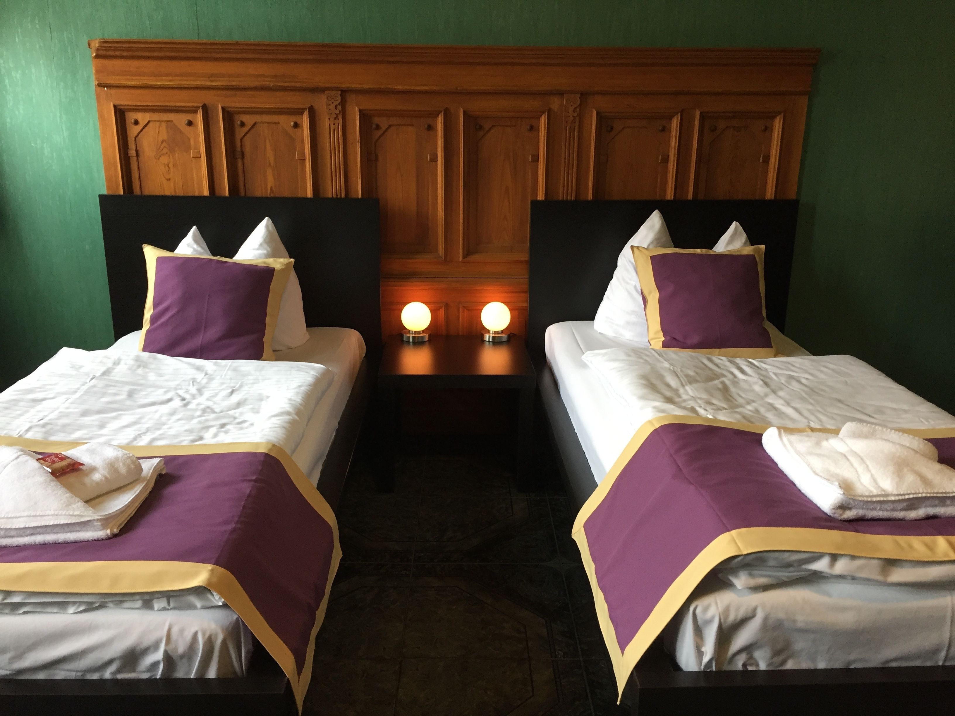 Two single beds with headboards, a nightstand with two illuminated lamps, and a green wall.
