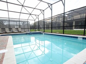 An indoor swimming pool with a clear view of the surrounding area, including a covered patio with lounge chairs and a grassy lawn. - Ov3019 - Champions Gate Resort - 9 Bed 5 Baths Villa (Davenport)