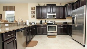 Una cocina moderna con gabinetes oscuros, electrodomésticos de acero inoxidable, encimeras de granito y lavavajillas.