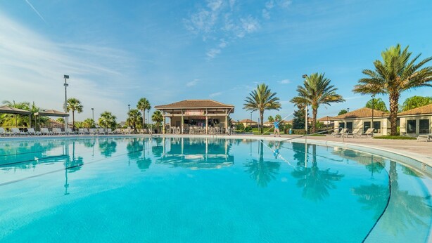 Una amplia piscina exterior con tumbonas y palmeras, rodeada de edificios de estilo mediterráneo.