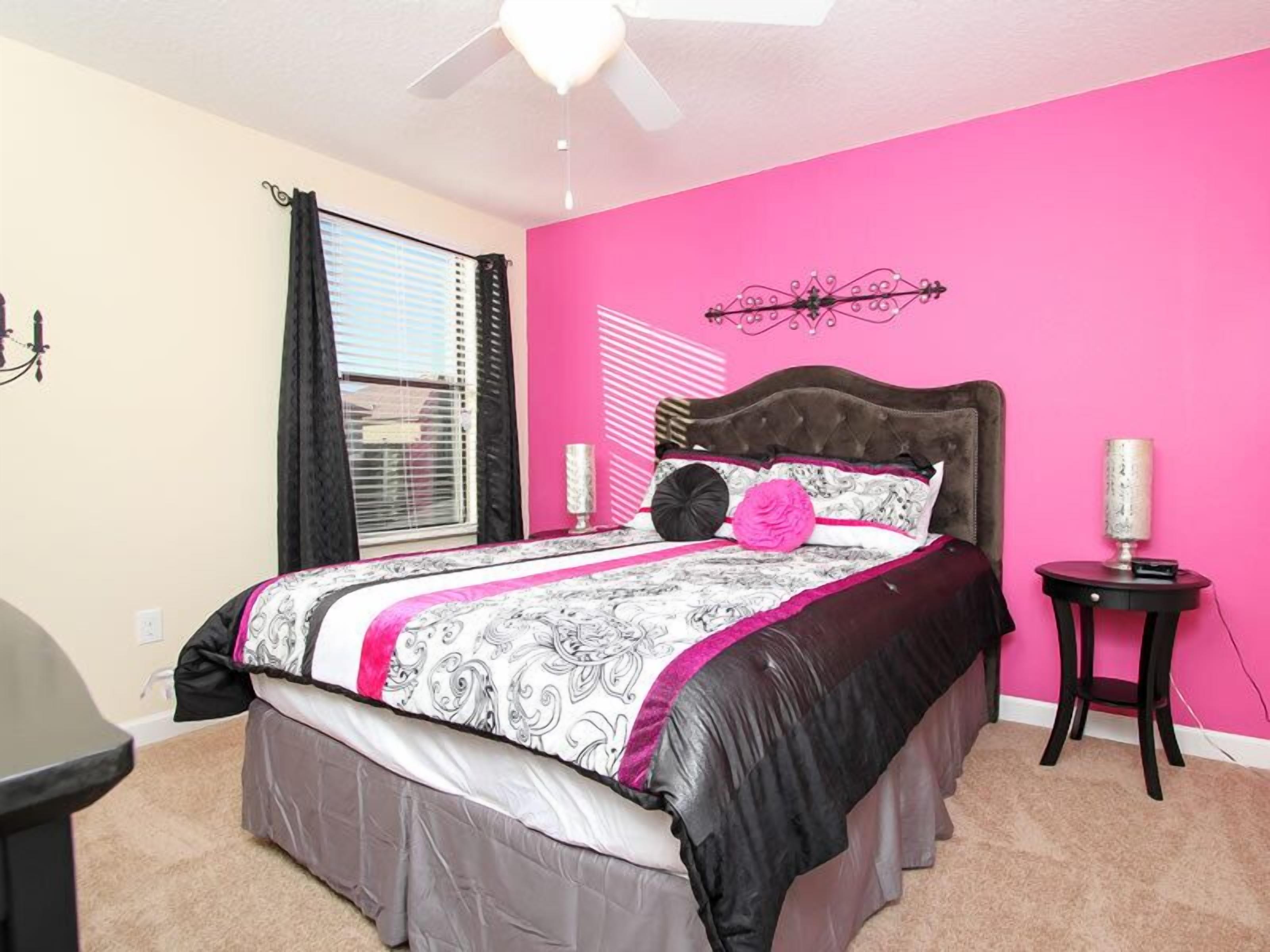 A bedroom with a bed, a ceiling fan, a window with blinds, a nightstand, and a lamp.